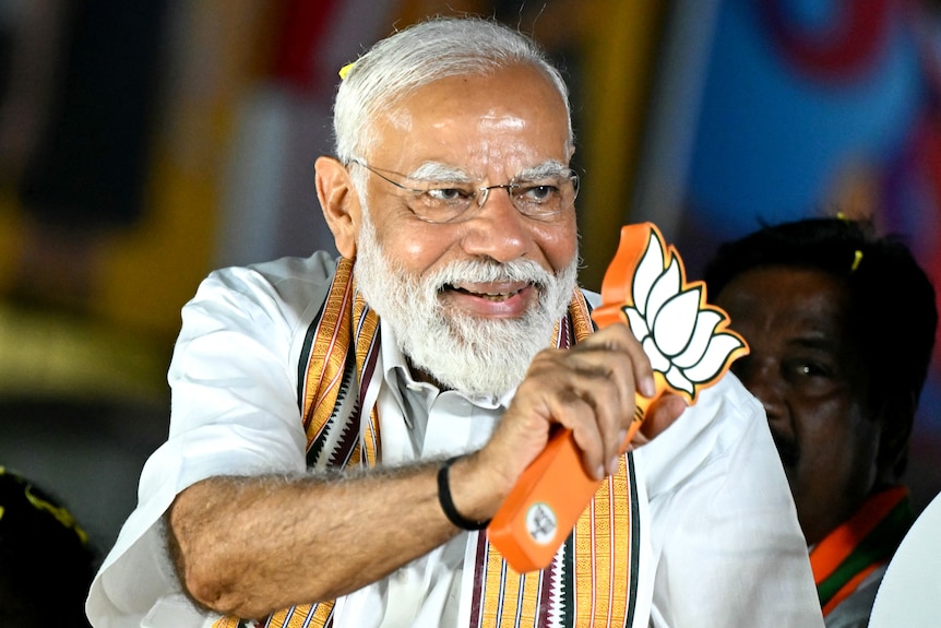 Narendra Modi smiles as he waves a stylised lotus leaf symbol.