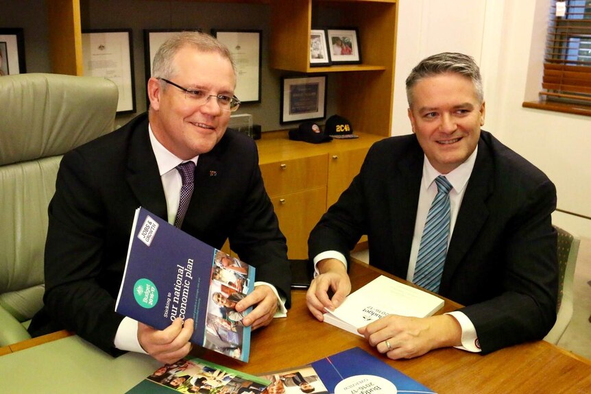 Scott Morrison and Mathias Cormann sit at a table with the budget papers in an office in Parliament House.