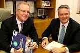 Scott Morrison and Mathias Cormann sit at a table with the budget papers in an office in Parliament House.