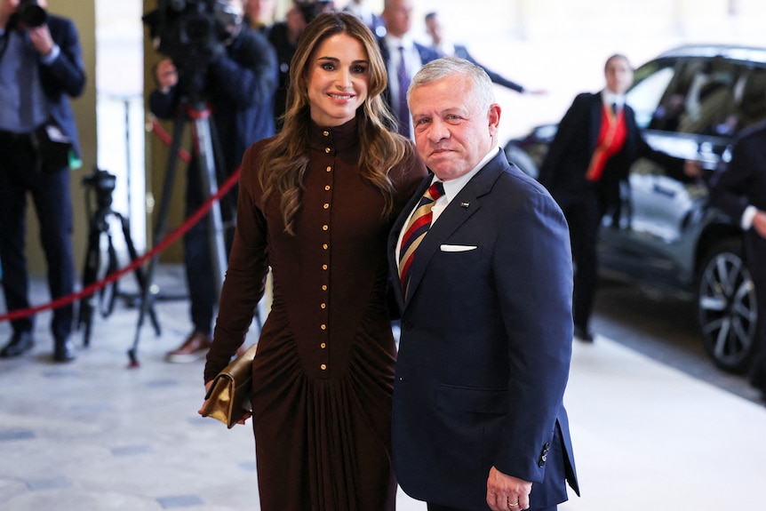 Queen Rania Al Abdullah and King Abdullah II stand in formal wear outside a function.