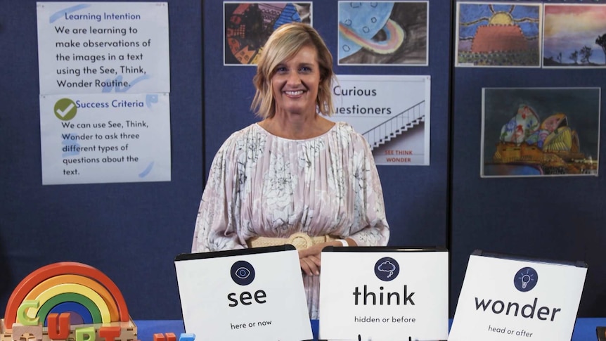 Female teacher stands in front of small posters with words "see", "think", "wonder"