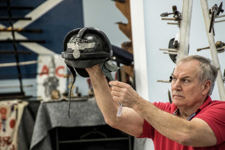 A man holds up a German motorcycle helmet to show a crowd at an auction.