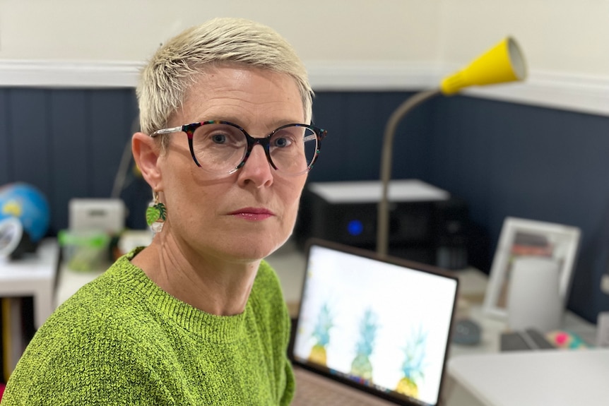 a woman with croped blonde hair looks into the camera while sitting at an office desk