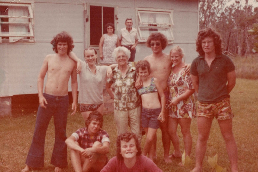 A family photo taken in the 1970s of a family with an elderley couple in the background.