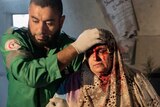 A Palestinian woman is helped by a paramedic out of her building, which was damaged during an Israeli air raid.