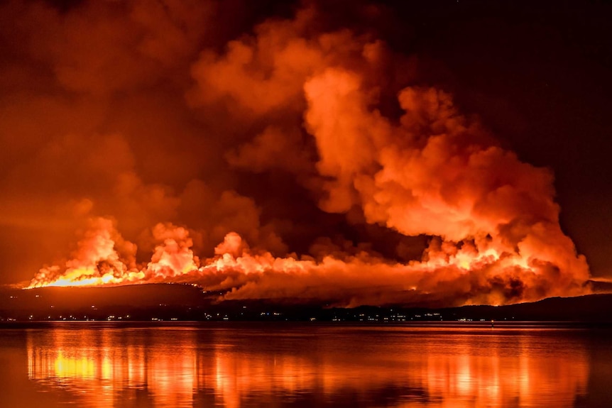 Bushfires burn on a hillside at night next to a body of water.