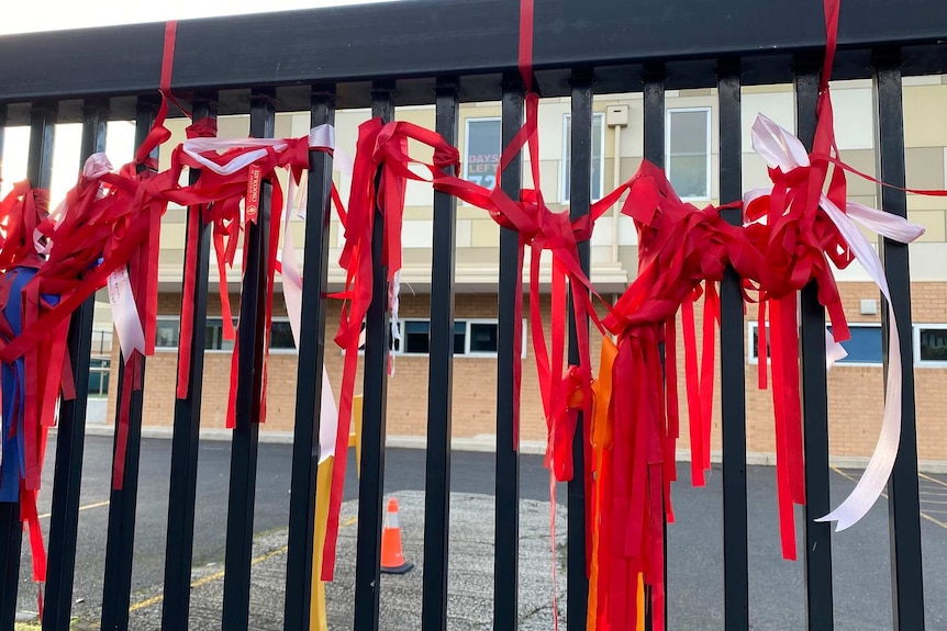 Bunches of red ribbons are tied to a school a closed school gate.