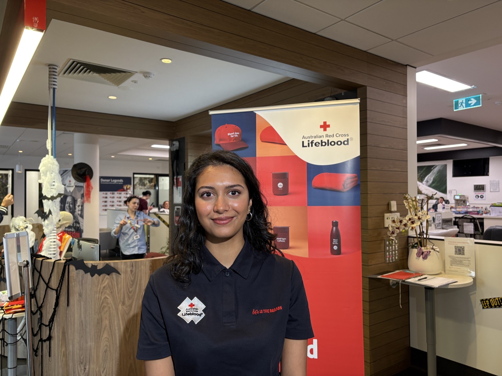 A young woman with black hair, smiles at the camera inside a blood donation centre