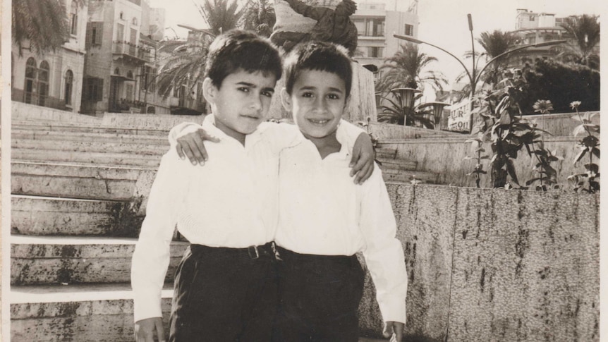 Two young boys stand with their arms around each other in a black and white image.