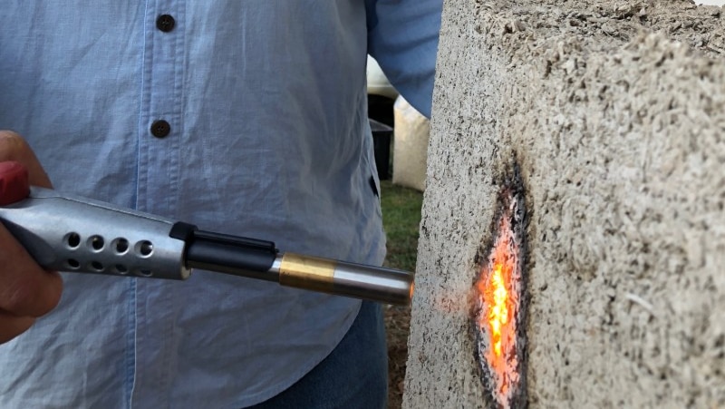A man holds a blowtorch flame to a panel of Hempcrete.
