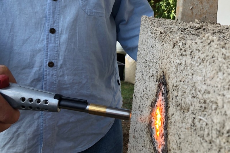 A man holds a blowtorch flame to a panel of building material.