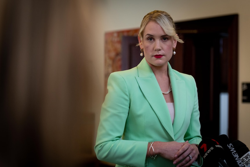 A blonde woman wearing a green jacket with looking stern