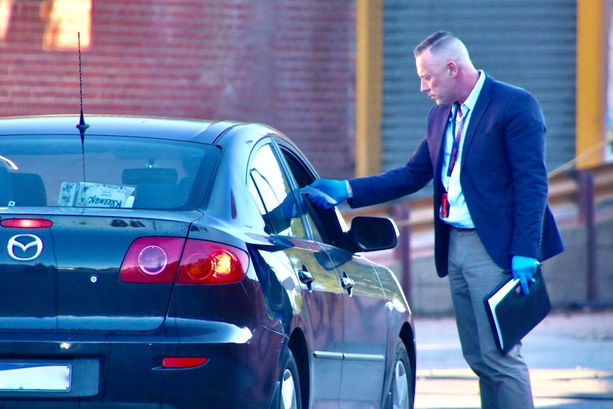 A person takes the temperature of a driver as they enter Cedar Meats in a black car.