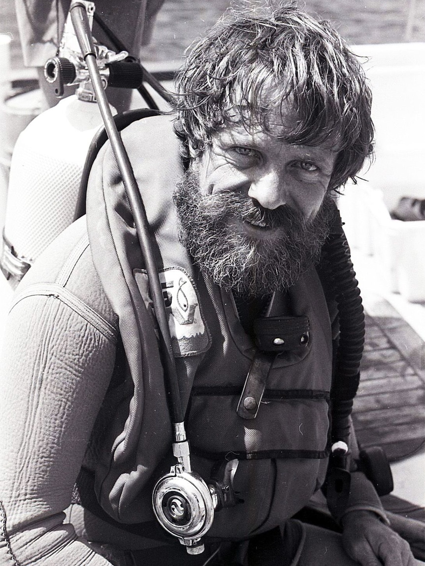 A black and white image of a man with beard in scuba gear, smiling