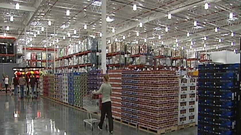 TV still of shoppers pushing trolleys past pallets on Costco floor