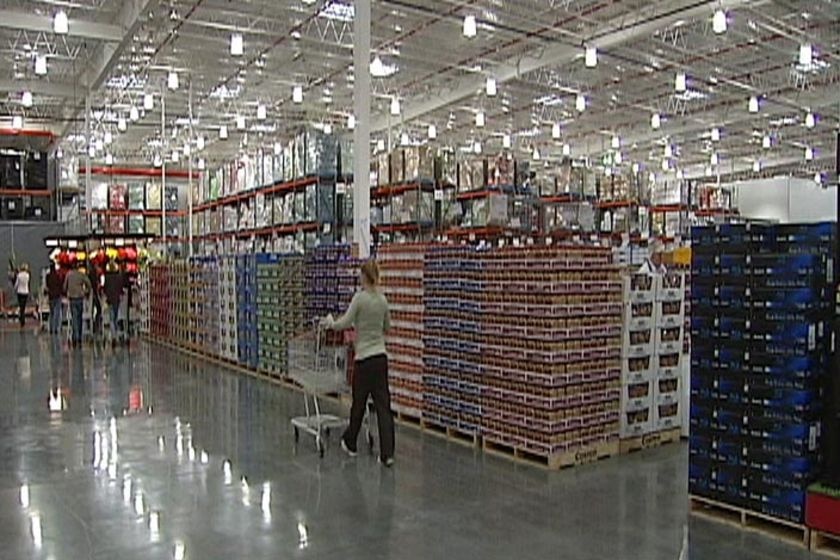 TV still of shoppers pushing trolleys past pallets on Costco floor