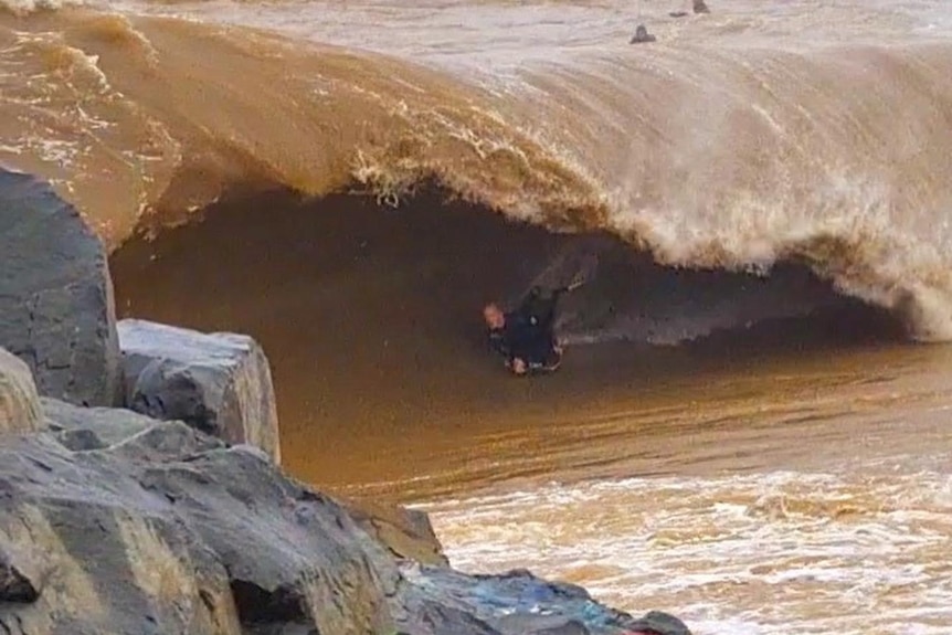 A wave with a thick lip and brown water, with a bodyboarder in the barrel of the wave.