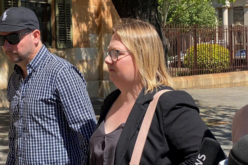 A woman with short blonde hair and glasses walking outside Adelaide's Magistrates Court. 