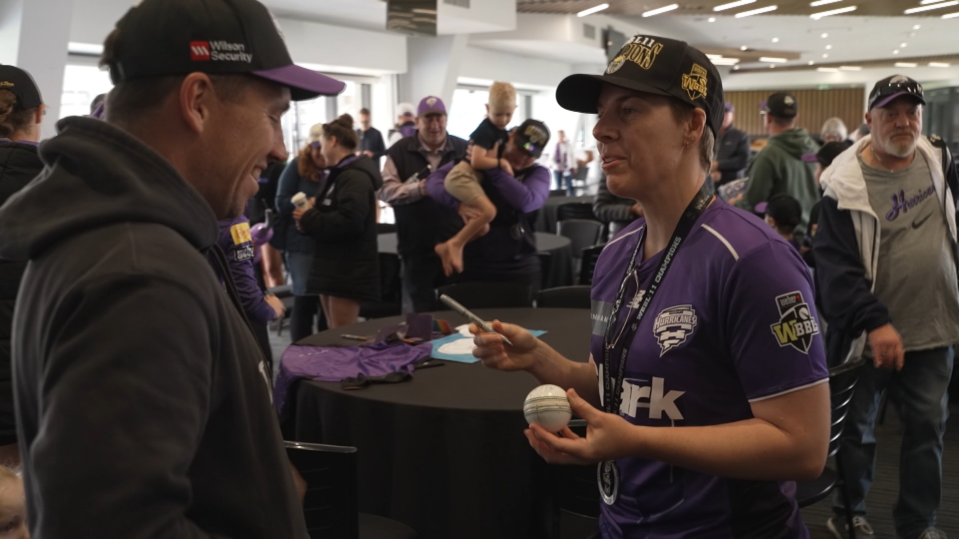 Elyse Villani, vestida con una camiseta y una gorra de los Hobart Hurricanes, firma un balón para un aficionado.