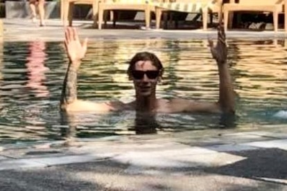 A young man with his arms raised, smiling broadly in a swimming pool.