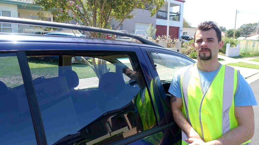 A young man on a suburban street standing next to his car.