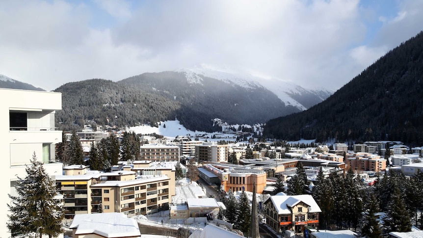 A town with a few apartment buildings set among snow-capped mountains.