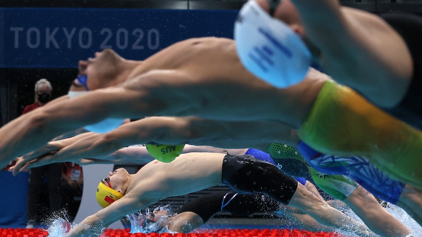 A row of eight backstroke swimmers dive into the water at the start of a mixed medley relay at the Tokyo Olympics.