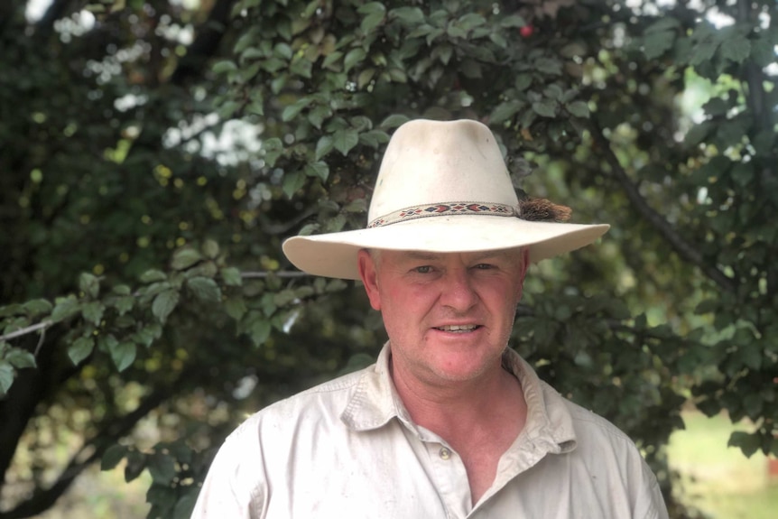 Man wearing a hat standing in front of a tree