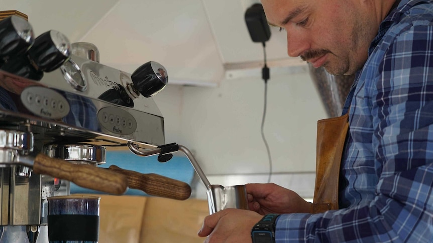 A man froths milk inside a coffee van