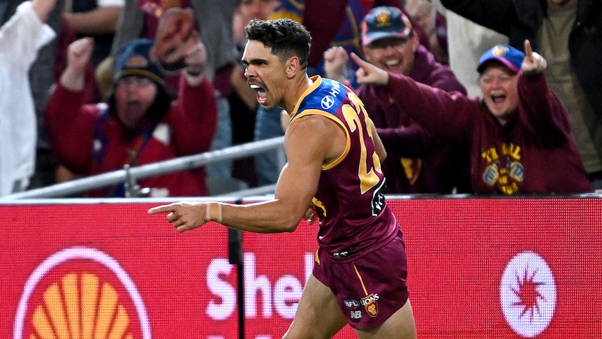 Brisbane Lions forward Charlie Cameron sprints away from goal, with his finger pointed in celebration as the crowd cheers. 