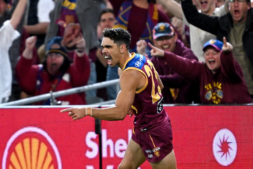 L'attaquant des Lions de Brisbane, Charlie Cameron, s'éloigne du but, le doigt pointé en guise de célébration tandis que la foule applaudit. 