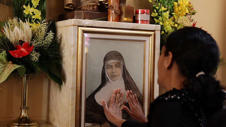 back view of woman placing her hands on the portrait of a nun, surrounded by flowers and candles