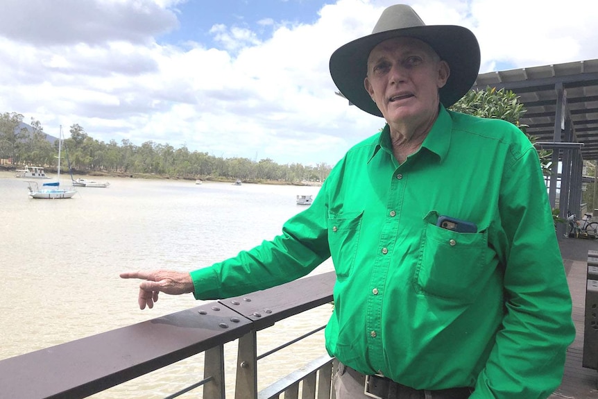 A man in a hat standing beside a railing on the banks of a river