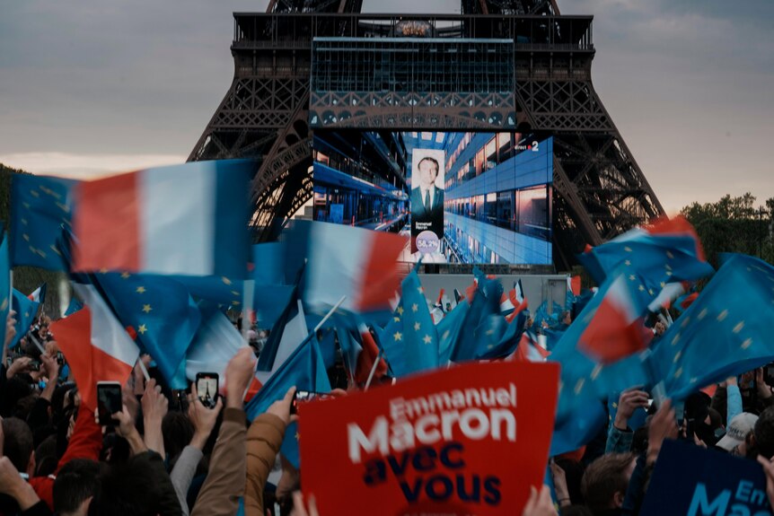 First election projections are shown on a screen in front of the Eiffel Tower in Paris.