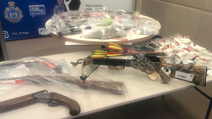 A crossbow and an array of plastic wrapped drugs, other weapons and cash displayed on tables.