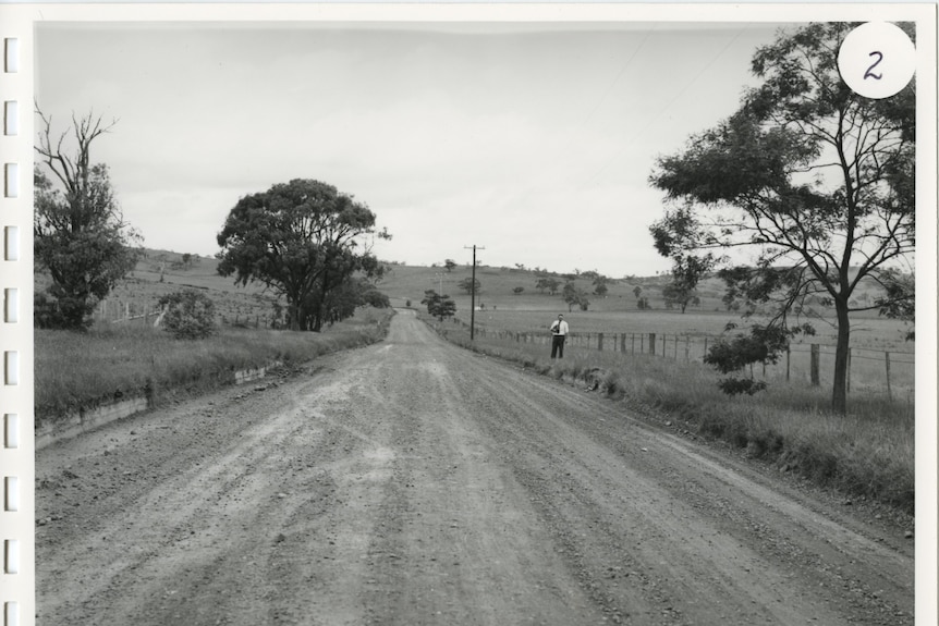 A man standing near a dirt road.