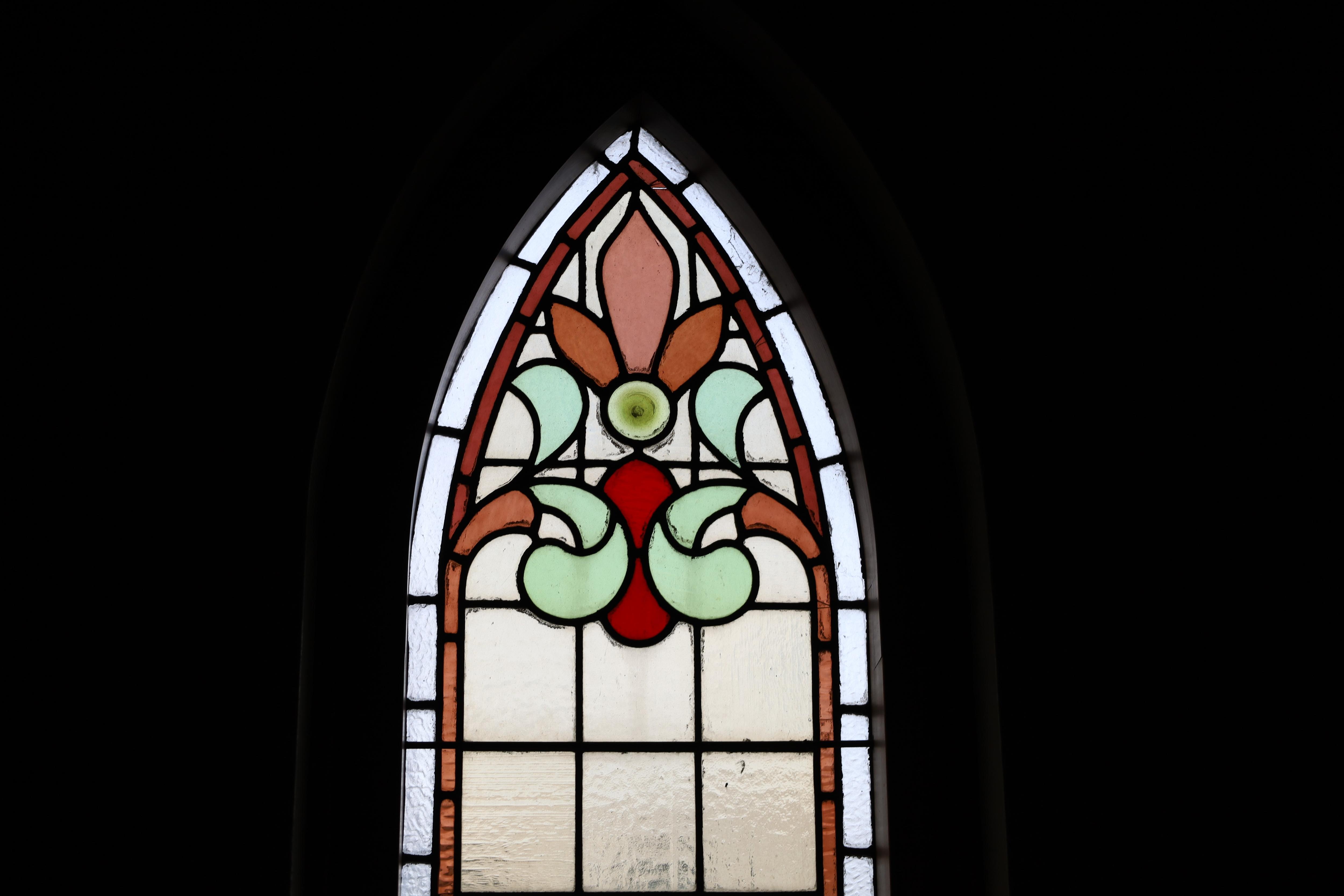 A stained glass church window with a decorative pattern in green, orange and red glass
