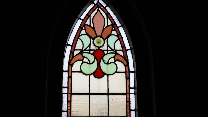 A stained glass church window with a decorative pattern in green, orange and red glass