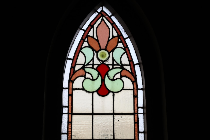 A stained glass church window with a decorative pattern in green, orange and red glass