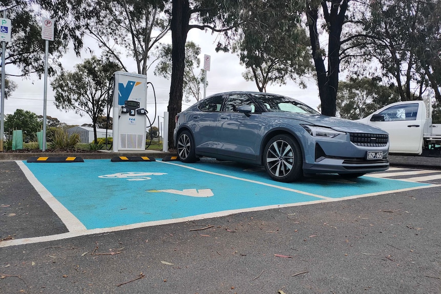 A blue electric vehicle is parked at an Evie charging station. The car park is painted blue.