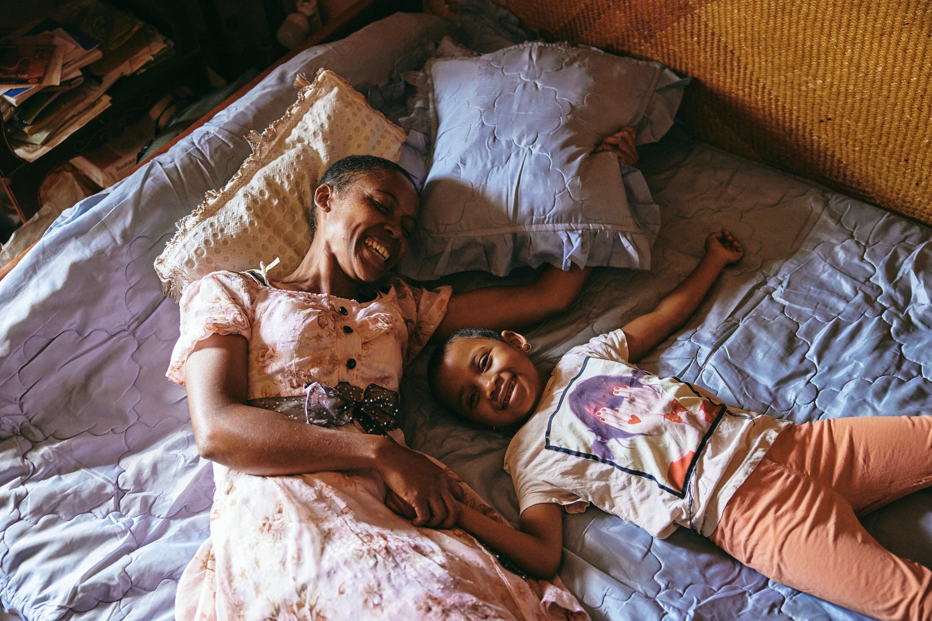 A mother and daughter lie on a bed laughing