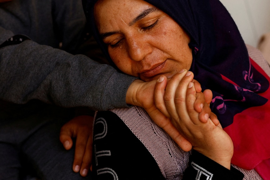 A woman holds a childs hand up to her face.