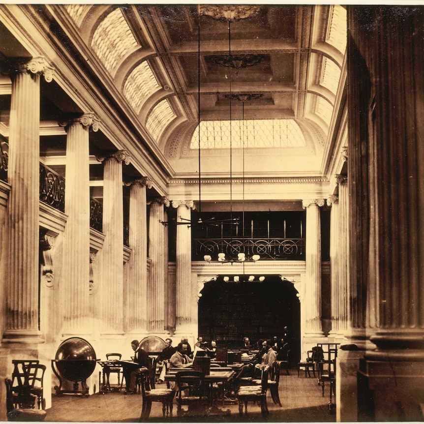A black and white photo of men sitting at wooden tables in the library hall taken in 1859.