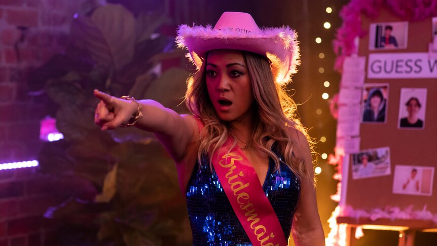 a woman wearing a pink cowboy hat is pointing past the camera, she looks surprised