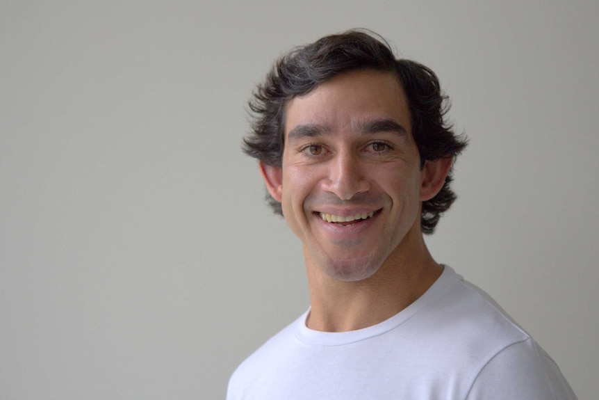 Dressed in a white t-shirt, Jonathan Thurston smiles against a beige background.