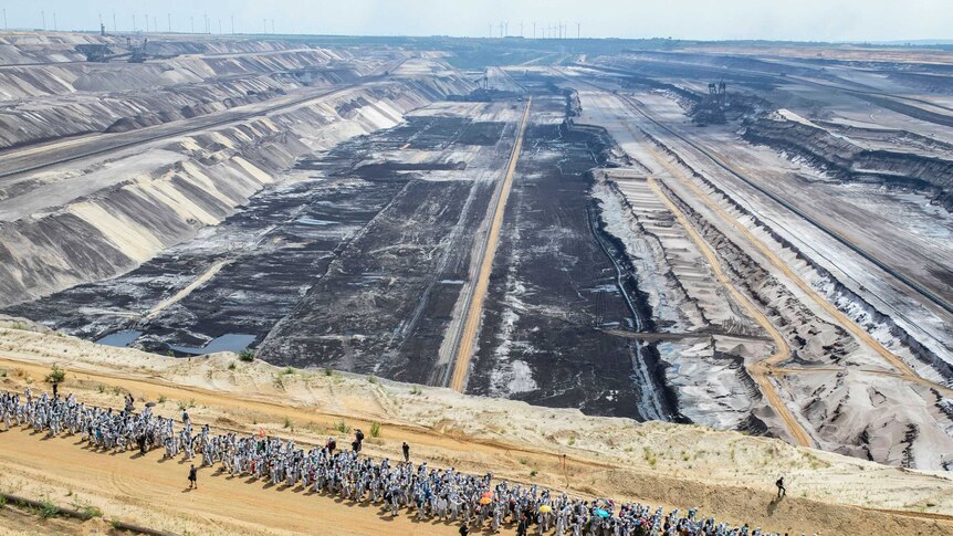 Hundreds of protesters walk in front of a huge open-cast mine.