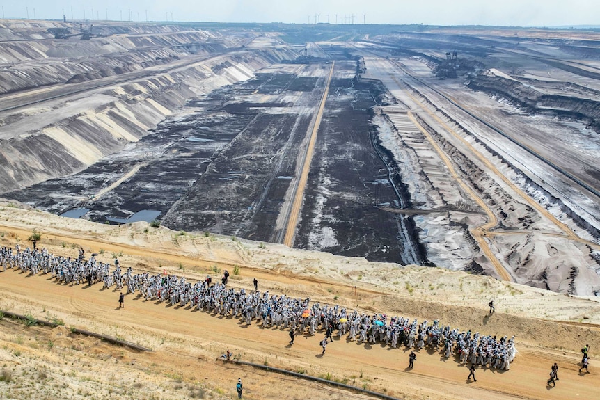 Hundreds of protesters walk in front of a huge open-cast mine.