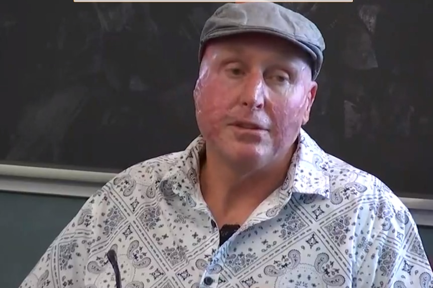 a man in a white shirt and grey hat sits in a chair