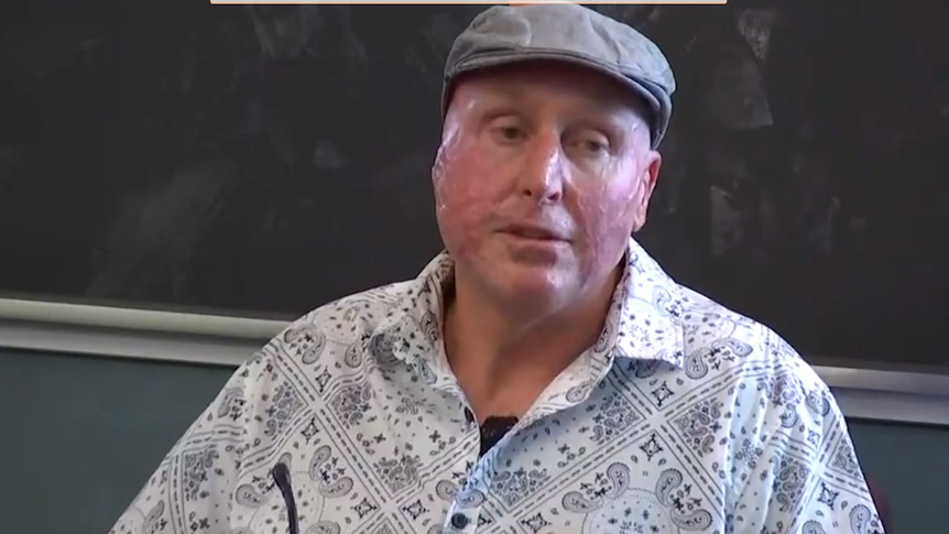 a man in a white shirt and grey hat sits in a chair