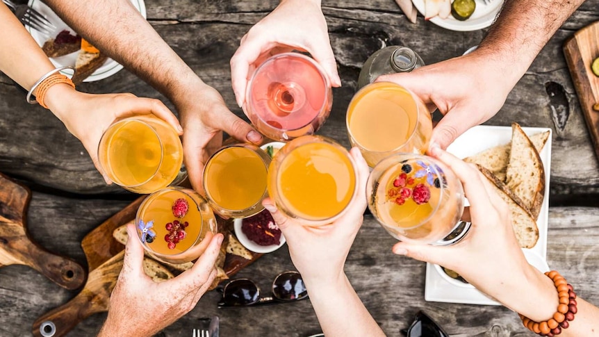 Hands holding different glasses of cider up together in a toast.